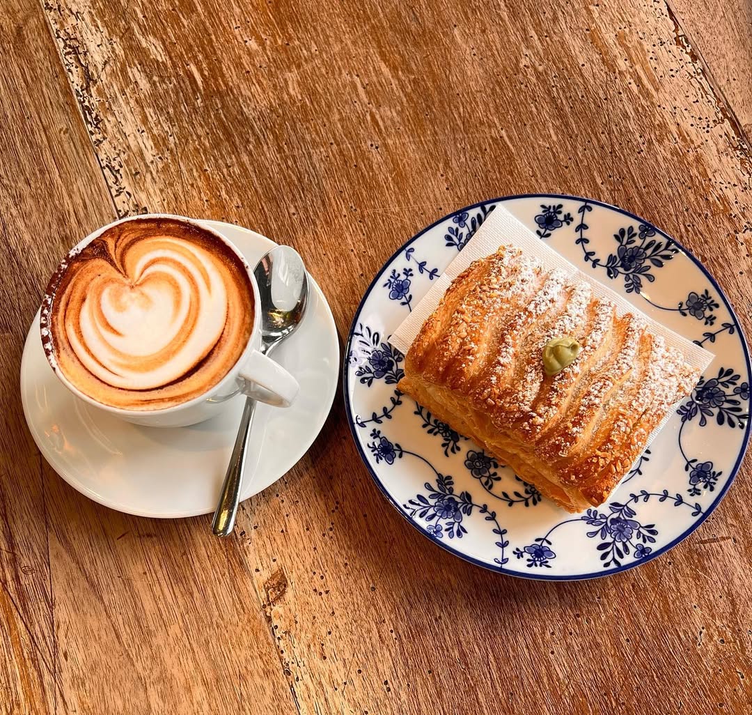 Cappuccino con latte art e saccottino al pistacchio su piatto blu