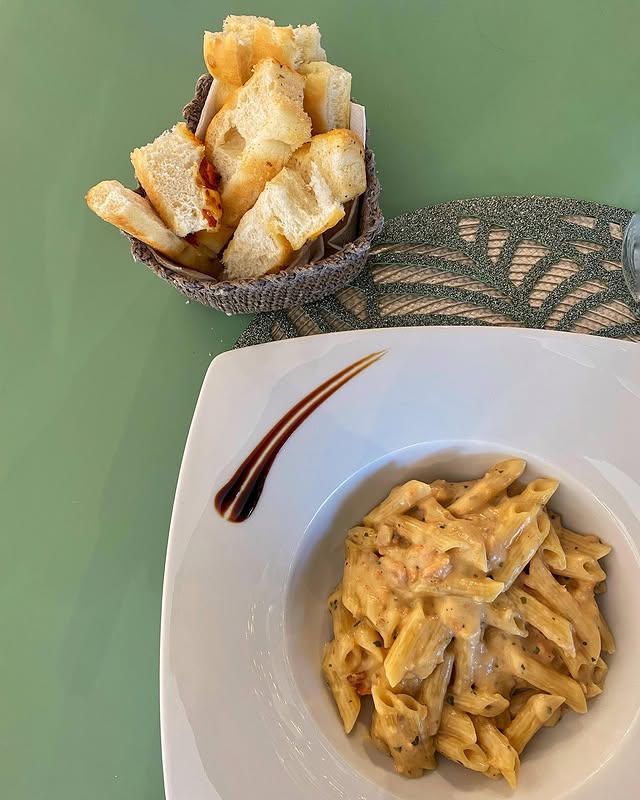Penne cremose con pane abbrustolito su sfondo verde salvia